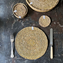 Load image into Gallery viewer, Round woven placemats on a dark surface with a fork and knife. | Hadley Green home