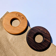 Load image into Gallery viewer, Two wooden clips one brown and one dark brown, on a paper bag with a light blue background. | Hadley Green Home