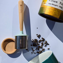 Load image into Gallery viewer, Tea-making tools including a wooden scoop, tea strainer, and a can of green tea leaves on a light blue background | Hadley Green Home