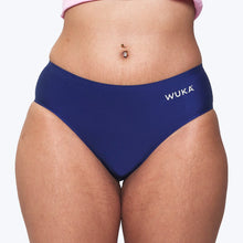 Load image into Gallery viewer, A close-up of a model wearing navy blue Period Pants with the brand name 'WUKA' printed in white on the right hip, set against a plain light gray background. | Hadley Green Home