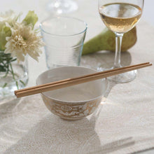 Load image into Gallery viewer, White bowl with gold patterns, wooden chopsticks, glass, and wine glass on a textured surface. | Little Twidlets 
