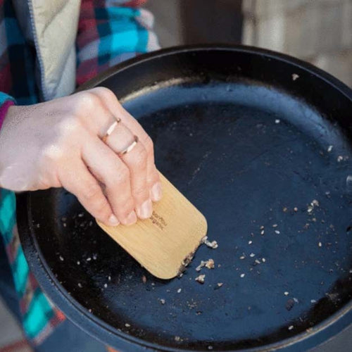 Person cleaning a black pan with a wooden scraper | Little Twidlets