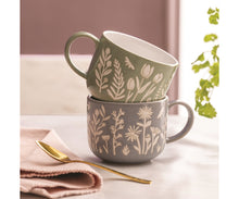 Load image into Gallery viewer, Two ceramic mugs stacked on a tabletop, one sage green and one warm Blue, both decorated with cream botanical and insect motifs. A folded pink napkin and gold spoon sit beside them, with a softly blurred indoor background and green leaves at the right edge. | Hadley Green Home 
